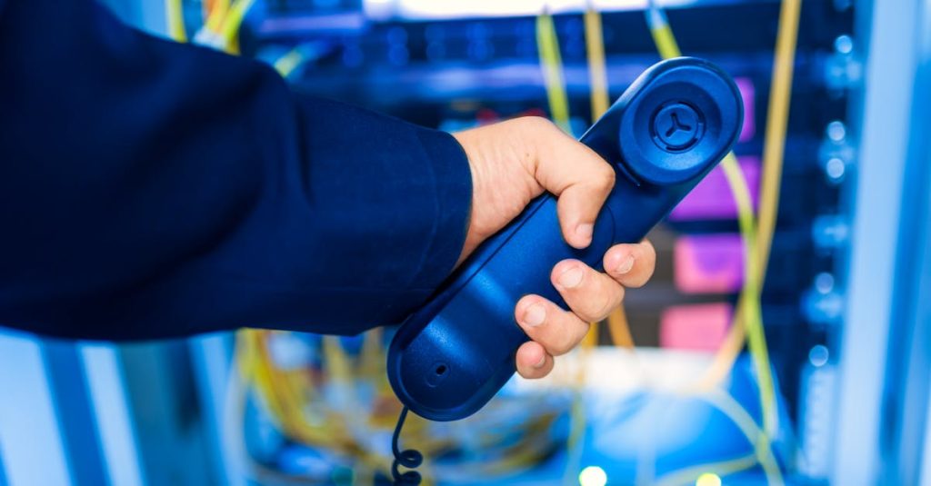 Close-up of a hand holding a telephone receiver in a server room emphasizing technology.